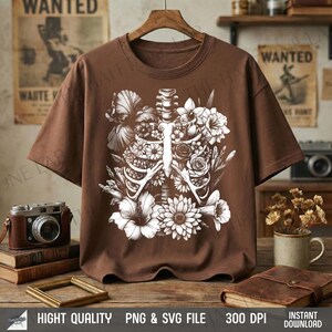 May include: A brown t-shirt featuring a white floral and rib cage design. The graphic includes various flowers and foliage, creating a unique and artistic aesthetic. The shirt is displayed on a wooden hanger.