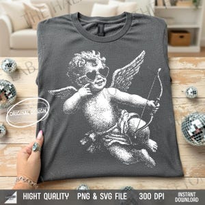 May include: Dark gray t-shirt featuring a white illustration of Cupid with heart-shaped sunglasses, wings, and a bow and arrow. The shirt has the text "ORIGINAL DESIGN" and "HIGHT QUALITY PNG & SVG FILE 300 DPI INSTANT DOWNLOAD".