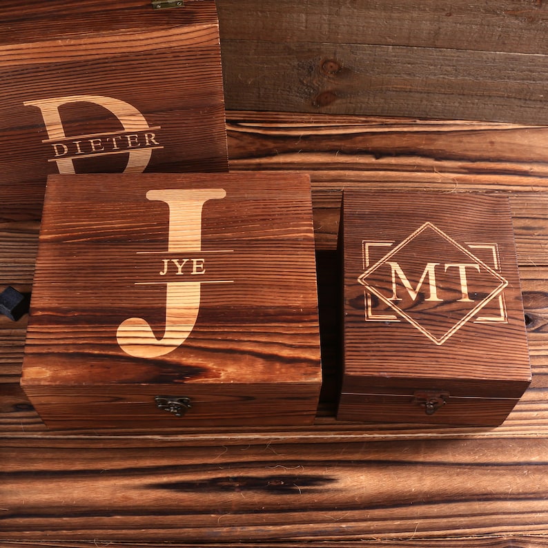 May include: Wooden boxes with engraved initials and names. The boxes are various sizes and have a dark brown finish. One box has the letter "J" with the name "JYE" below it. Another box has the initials "MT" inside a diamond.