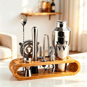 Op de afbeelding: Een roestvrijstalen cocktailshaker-set met een houten standaard. De shaker is voorzien van de tekst Warner en de letter W. De set bevat een menglepel, zeef, stamper, jigger, schenktuit, tang en kurkentrekker, georganiseerd in een bamboe houder.