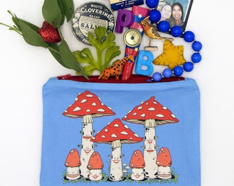 Puede incluir: Una bolsa azul con cremallera con un diseño caprichoso de setas rojas y blancas con caras sonrientes. La bolsa está llena de varios artículos, incluyendo un collar de cuentas azules, una pequeña lata de sal, una jirafa de juguete, un pájaro de juguete y una caja vintage de una empresa de vidrio.