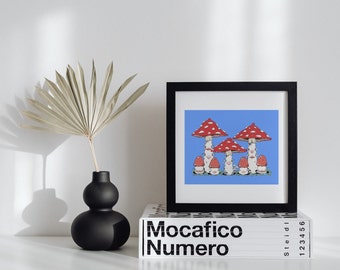 Puede incluir: Una impresión enmarcada en negro con un fondo azul que presenta un grupo de setas rojas y blancas con caras sonrientes. La impresión está colocada encima de una pila de libros con el texto "Mocafico Numero" impreso en la parte delantera.