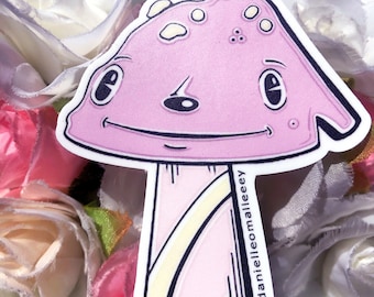 Puede incluir: Una pegatina de hongo rosa con una cara sonriente y manchas blancas. El tallo es rosa y blanco con contornos negros. La pegatina tiene el texto "@danielleomalley" en la parte inferior.