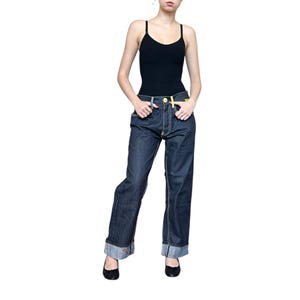 May include: Dark wash denim jeans with a yellow accent on the belt loop and cuffs. The jeans have a relaxed fit and are paired with a black camisole. The cuffs are rolled up, revealing a floral pattern.