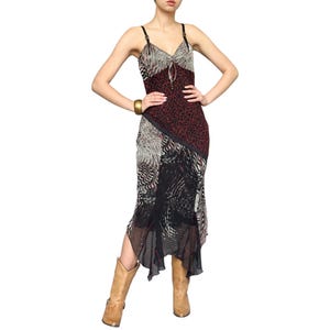 Pode incluir: Vestido estampado com decote em V e alças finas. O vestido apresenta uma mistura de estampas de animais em tons de vermelho, preto e cinza. O vestido é combinado com botas de cowboy castanhas.