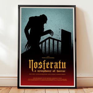 Może przedstawiać: Oprawiony plakat z czarną sylwetką stworzenia z długimi palcami na niebieskim tle. Tytuł "Nosferatu" jest złotymi literami, z napisem "a symphony of horror" poniżej. Plakat jest w czarnej ramie.