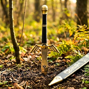 Peut inclure: Une &eacute;p&eacute;e en m&eacute;tal avec une poign&eacute;e envelopp&eacute;e de noir, un pommeau dor&eacute; et une garde dot&eacute;e d'extensions en forme d'ailes. La lame est argent&eacute;e avec un petit embl&egrave;me triangulaire pr&egrave;s de la garde, accompagn&eacute;e d'un fourreau noir aux d&eacute;tails dor&eacute;s.