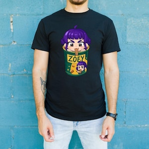 May include: Black t-shirt featuring a cartoon graphic of a purple-haired character in a green cup with the name "ZOEY". The design includes a smaller version of the character and the cup. The shirt is worn by a person.