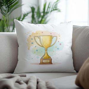 May include: White throw pillow featuring a gold trophy illustration. The trophy is set against a watercolor background with colorful stars. The pillow is on a gray sofa, with a plant in the background.