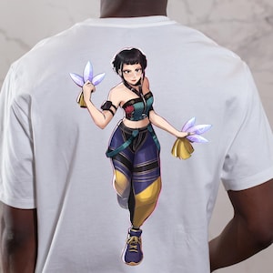 May include: White t-shirt featuring a colorful anime-style illustration of a female character. The character is depicted in a dynamic pose, holding glowing objects. The design incorporates shades of blue, yellow, and purple, creating a vibrant aesthetic.