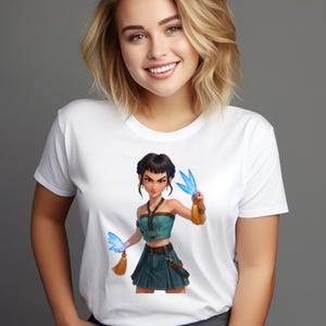 May include: White t-shirt featuring a digital illustration of a woman in a teal crop top and skirt, holding blue, wing-shaped objects. The illustration has a fantasy theme with gold accents and a determined expression.