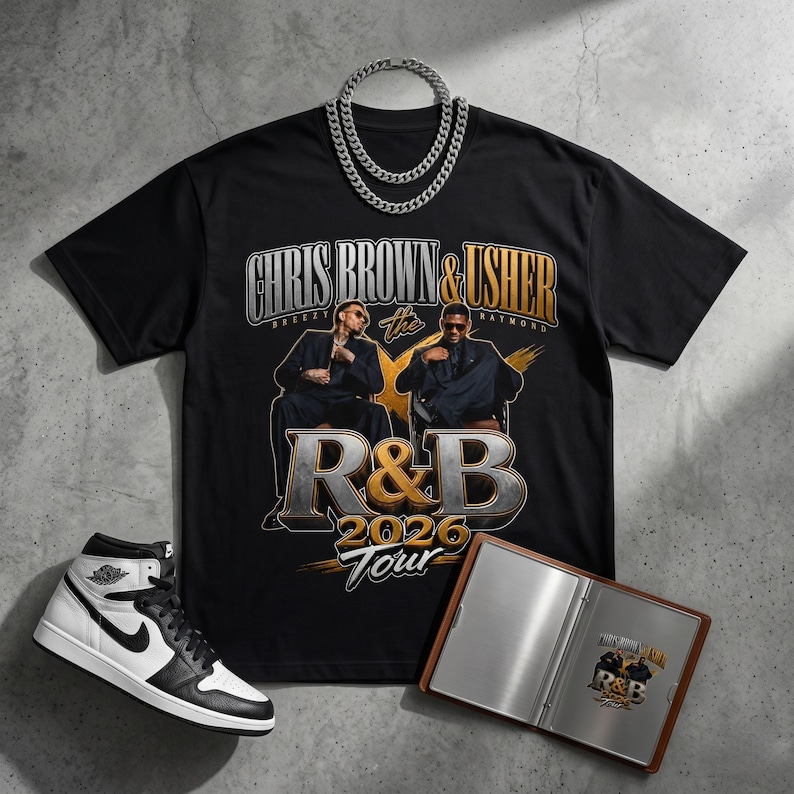 May include: Black t-shirt with a Chris Brown & Usher R&B 2026 Tour graphic, a silver chain, and a pair of black and white trainers. A small brown notebook with a silver interior is also present.
