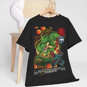 May include: Black t-shirt featuring a green dragon illustration with orange orbs and Japanese text. The design includes the text "MASTERMIND" and "ドラゴンボール". A white baseball cap hangs on a wooden chair in the background.
