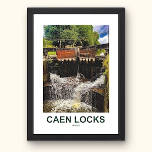 Puede incluir: Impresión enmarcada de las esclusas de Caen en Devizes. La imagen muestra agua cayendo en cascada sobre las esclusas, con estructuras de ladrillo y piedra. La parte superior de la imagen muestra árboles verdes y un cielo azul. El texto "CAEN LOCKS" está impreso en la parte inferior.