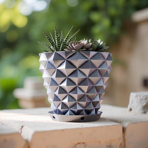 Può includere: Fioriera geometrica con finitura metallica e motivo triangolare, contenente una varietà di piante grasse. La fioriera è grigia con accenti argentati e poggia su un sottovaso abbinato.