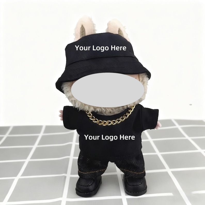 K&ouml;nnte beinhalten: Ein Pl&uuml;schtier in einem schwarzen Outfit, einschlie&szlig;lich eines Fischerhuts, T-Shirts und Jeans. Der Hut und das Shirt zeigen den Text "Your Logo Here". Eine goldene Kette und schwarze Schuhe vervollst&auml;ndigen den Look.