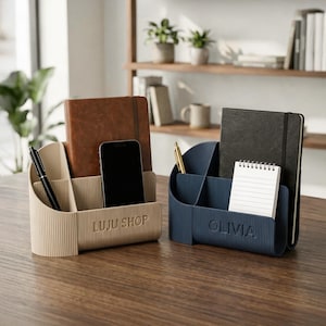 May include: Two desk organizers, one beige and one navy blue, each with multiple compartments. The beige organizer has "LUJU SHOP" printed on it, and the navy blue organizer has "OLIVIA" printed on it. Both hold notebooks, pens, and a smartphone.