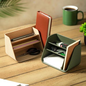 May include: Two tiered desk organizers in beige and olive green with ribbed side panels. The beige organizer holds a pen, pencils, scissors, and a tall notebook. The olive green organizer contains binder clips, an eraser, and a spiral notebook.