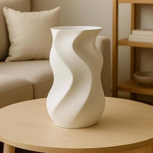 May include: A white ceramic vase with a unique, wavy design. The vase has a wide base that tapers to a narrower neck and flares out at the top. The vase is sitting on a round wooden table. Home decor.
