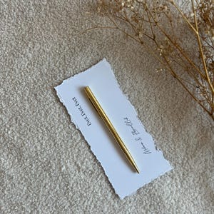 Pu&ograve; includere: Una penna in metallo dorato poggia in diagonale su un cartoncino rettangolare bianco con bordi irregolari. Il cartoncino riporta il testo stampato "Evet, Evet, Evet" e "Mihran & Efsun'un" in inchiostro nero. Un rametto di fiori secchi &egrave; posizionato a destra.