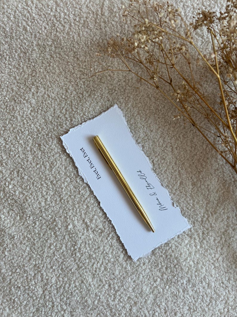 Pu&ograve; includere: Una penna in metallo dorato poggia in diagonale su un cartoncino rettangolare bianco con bordi irregolari. Il cartoncino riporta il testo stampato "Evet, Evet, Evet" e "Mihran & Efsun'un" in inchiostro nero. Un rametto di fiori secchi &egrave; posizionato a destra.