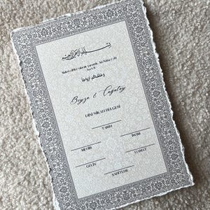 Pu&ograve; includere: Un certificato cartaceo rettangolare con bordi irregolari, caratterizzato da un bordo floreale grigio decorato. Il testo include 'Beyza & Cagatay', 'DINI NIKAH BELGESI' e linee per 'TARIH', 'IMAM', 'MEHIR', 'DAMAT', 'GELIN' e 'SAHITLER'.