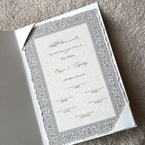 Pode incluir: Um convite ou certificado formal com detalhes cinza e branco ornamentados. O documento apresenta escrita &aacute;rabe e os nomes Beyza & Cagatay. As bordas t&ecirc;m uma borda decorativa e texturizada. O fundo &eacute; cinza claro.