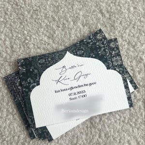 May include: Stack of invitation cards with a white textured front and a dark green patterned back. The front of the card has text in a script font. The text includes the date 07.11.2025 and time 17:00.