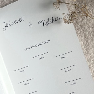 Może przedstawiać: Biały dokument papierowy zatytułowany Dini Nikah Belgesi z imionami G&uuml;lsever & Metehan u g&oacute;ry. Zawiera puste linie na Tarih, Imam, Mehir, Damat, Gelin i Sahit oraz tekst Sizleri ciftler olarak yarattik.
