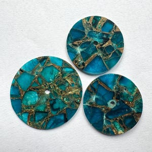 Può includere: Tre cabochon rotondi in pietra preziosa turchese con un motivo a mosaico di venature dorate. Ogni cabochon ha un piccolo foro al centro. Le pietre preziose sono su uno sfondo bianco.