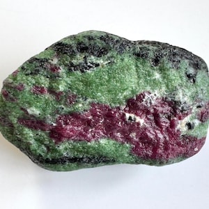 Könnte beinhalten: Ein naturbelassener Stein mit einer Mischung aus Farben. Der Stein zeigt eine grüne Basis mit Streifen in tiefem Rot und Schwarz. Die Textur ist körnig und natürlich, mit einer leicht unebenen Oberfläche.