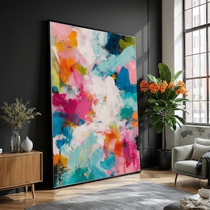 Könnte beinhalten: Großer, gerahmter Kunstdruck mit abstrakter Malerei. Das Kunstwerk zeigt kräftige Pinselstriche in leuchtenden Farben, darunter Rosa, Orange, Blau und Weiß. Das Gemälde wird in einem modernen Wohnzimmer vor einer dunklen Wand präsentiert.