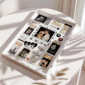 Puede incluir: Una caja blanca con varios recuerdos, incluyendo fotograf&iacute;as, cajas de cerillas, dados y amuletos en forma de coraz&oacute;n. Las fotos muestran parejas bes&aacute;ndose. Las cajas de cerillas tienen ilustraciones de un perro, la luna y el horizonte de Nueva York.