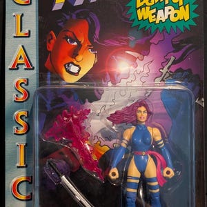 May include: X-Men Classics Psylocke action figure in original packaging. The figure is in a blue and yellow bodysuit with a pink sash and purple hair. Includes a light-up psychic knife. The packaging features the Marvel Comics logo.