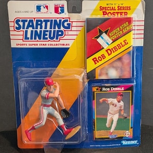 May include: A Starting Lineup sports collectible featuring a baseball player figurine, a poster, and a trading card. The packaging includes the text "Starting Lineup" and "Rob Dibble". The figurine is of a baseball pitcher in a red and gray uniform.