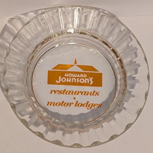 May include: Clear glass ashtray with a ridged outer edge. The center features the Howard Johnson's logo in orange and the words "restaurants" and "motor lodges" in orange text.