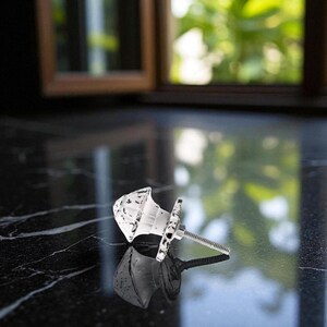 May include: White and black distressed cabinet knob with a decorative design. The knob is made of a light-colored material and features a black speckled pattern. The knob is attached to a metal screw.