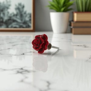 May include: A red rose-shaped cabinet knob with a silver screw. The decorative knob is made of ceramic and is set against a white marble surface. The rose has detailed petals and a glossy finish.