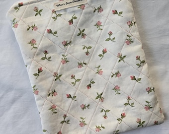 Puede incluir: Una funda acolchada con cremallera de color crema, adornada con un estampado floral de rosas rosas y hojas verdes. La funda presenta un diseño de costura de diamante y una etiqueta que dice "Wren's Sewn Treasures".