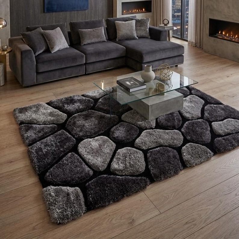 May include: A rectangular area rug featuring a textured, multi-tonal grey and charcoal pattern of irregular, stone-like shapes separated by black lines. The rug has a high-pile, shaggy surface and is positioned on a light-coloured wooden floor.