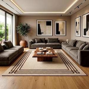 May include: A living room featuring a large sectional sofa in dark grey fabric, a natural wood coffee table with a live edge, and a beige area rug with dark brown geometric border lines. Four framed abstract art pieces hang on the wall.
