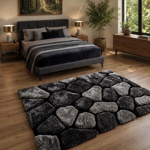 May include: A rectangular area rug featuring a high-pile, textured design of interlocking stone-like shapes in varying shades of charcoal, slate grey, and silver. The rug has a thick, plush surface that mimics the appearance of a cobblestone path.
