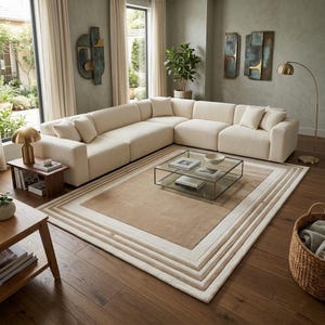 May include: A large cream-coloured sectional sofa with matching throw pillows, positioned on a rectangular area rug featuring concentric tan and white borders. A glass coffee table sits in the centre, accompanied by a gold floor lamp and side table.