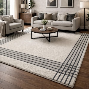May include: A cream-coloured rectangular rug with a dark grey border. The border design features parallel lines intersecting at the corners, forming a geometric pattern. The rug is placed on a wooden floor, suitable for a living room.