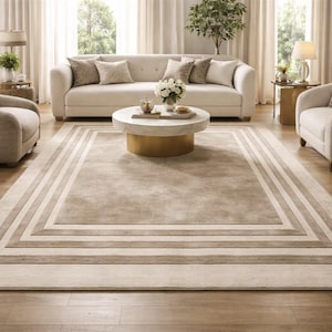 May include: A living room with a large, neutral-toned rug with a bordered design. A cream-coloured sofa with cushions sits in front of a window. A round coffee table and two armchairs are also visible.