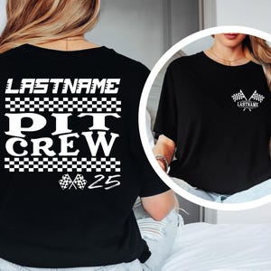 Op de afbeelding: Zwart T-shirt met witte tekst en geblokte vlagafbeeldingen. De tekst op de achterkant luidt "LASTNAME PIT CREW 25". Een kleinere afbeelding toont de voorkant met vlaggen en de naam.