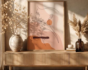 Könnte beinhalten: Ein gerahmter Wandkunstdruck mit einer durchgehenden schwarzen Linienzeichnung eines Gesichts vor einem Hintergrund aus abstrakten Formen in Pfirsich-, Terrakotta- und Cremetönen, mit einem dunkelbraunen Pinselstrich-Akzent.