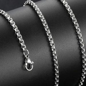 May include: A silver-toned box chain necklace featuring a polished metallic finish and a secure lobster claw clasp. The chain consists of interconnected square links that create a smooth, uniform, and continuous cylindrical appearance throughout.