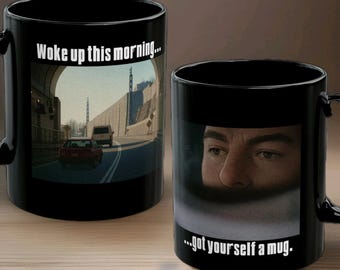 May include: Two black ceramic mugs with a humorous design. One mug features a road scene with the text "Woke up this morning...". The other mug displays a man's face with the text "...got yourself a mug."