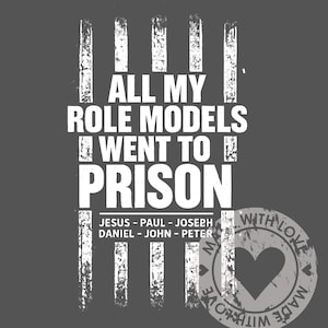 May include: A dark gray graphic design with white text that reads "ALL MY ROLE MODELS WENT TO PRISON." Below the text are the names "JESUS - PAUL - JOSEPH, DANIEL - JOHN - PETER." A circular stamp with a heart and the words "MADE WITH LOVE" is in the lower right.
